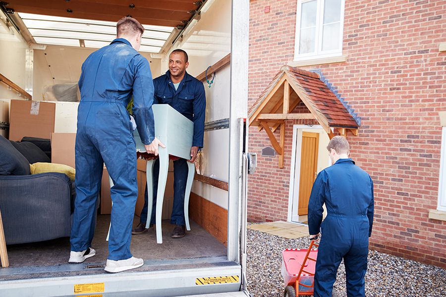 Moving Company Insurance - Moving Company Workers Unloading Furniture And Boxes From Truck Into New Home On Moving Day